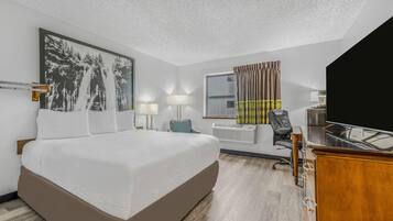 Habitación de hotel con una cama grande, dos lámparas de noche, un escritorio con una computadora, una silla y un amplio ventanal con cortinas.
