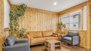 Una habitación acogedora con un revestimiento de madera, un sofá de cuero marrón, un sillón gris y una mesa de centro de madera.