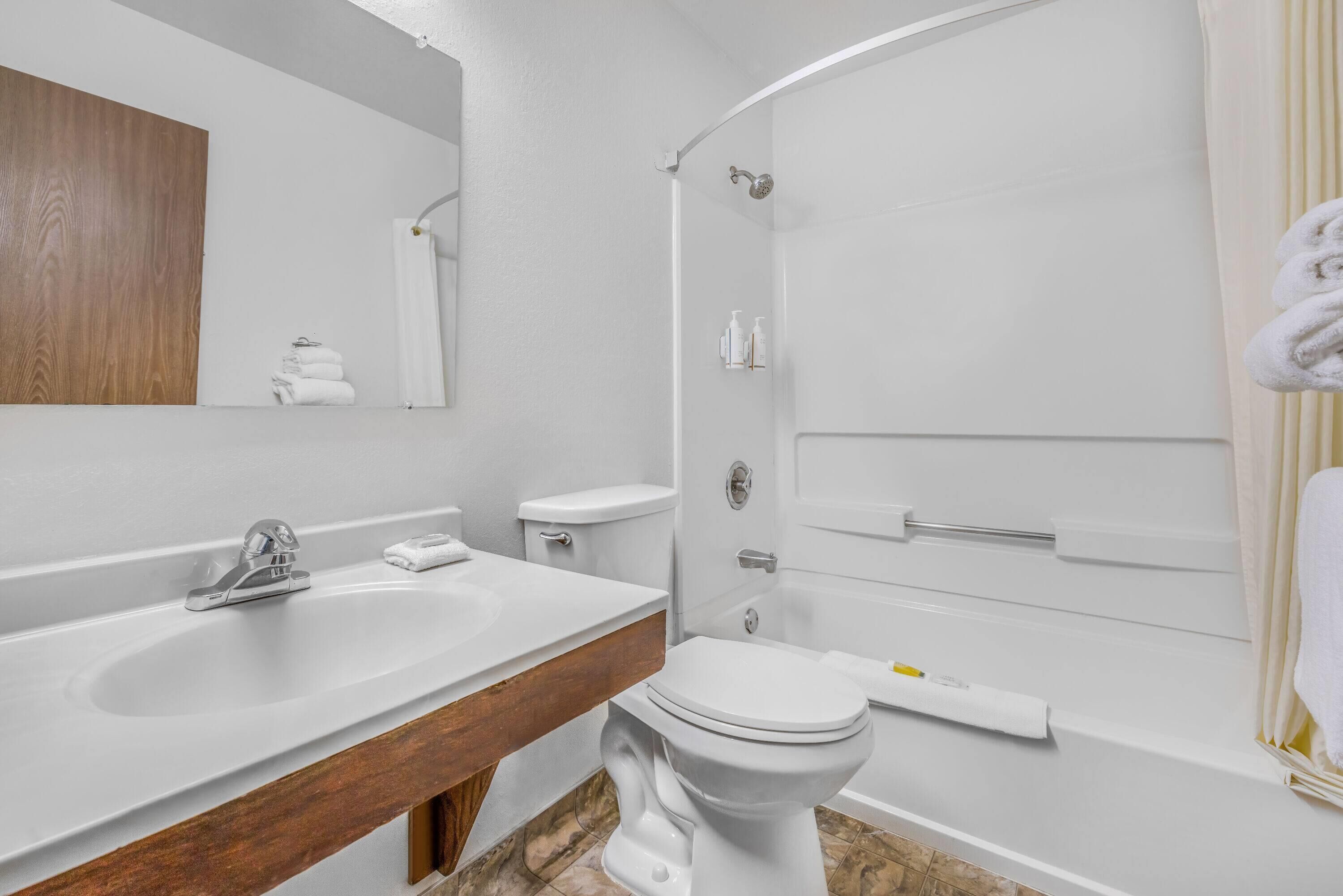Un baño moderno con un lavamanos blanco, tocador de madera, inodoro y zona de ducha.