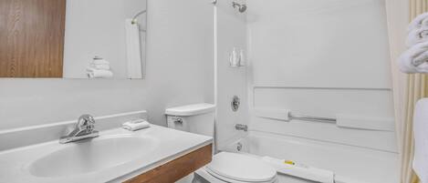 Un baño moderno con un lavamanos blanco, tocador de madera, inodoro y zona de ducha.