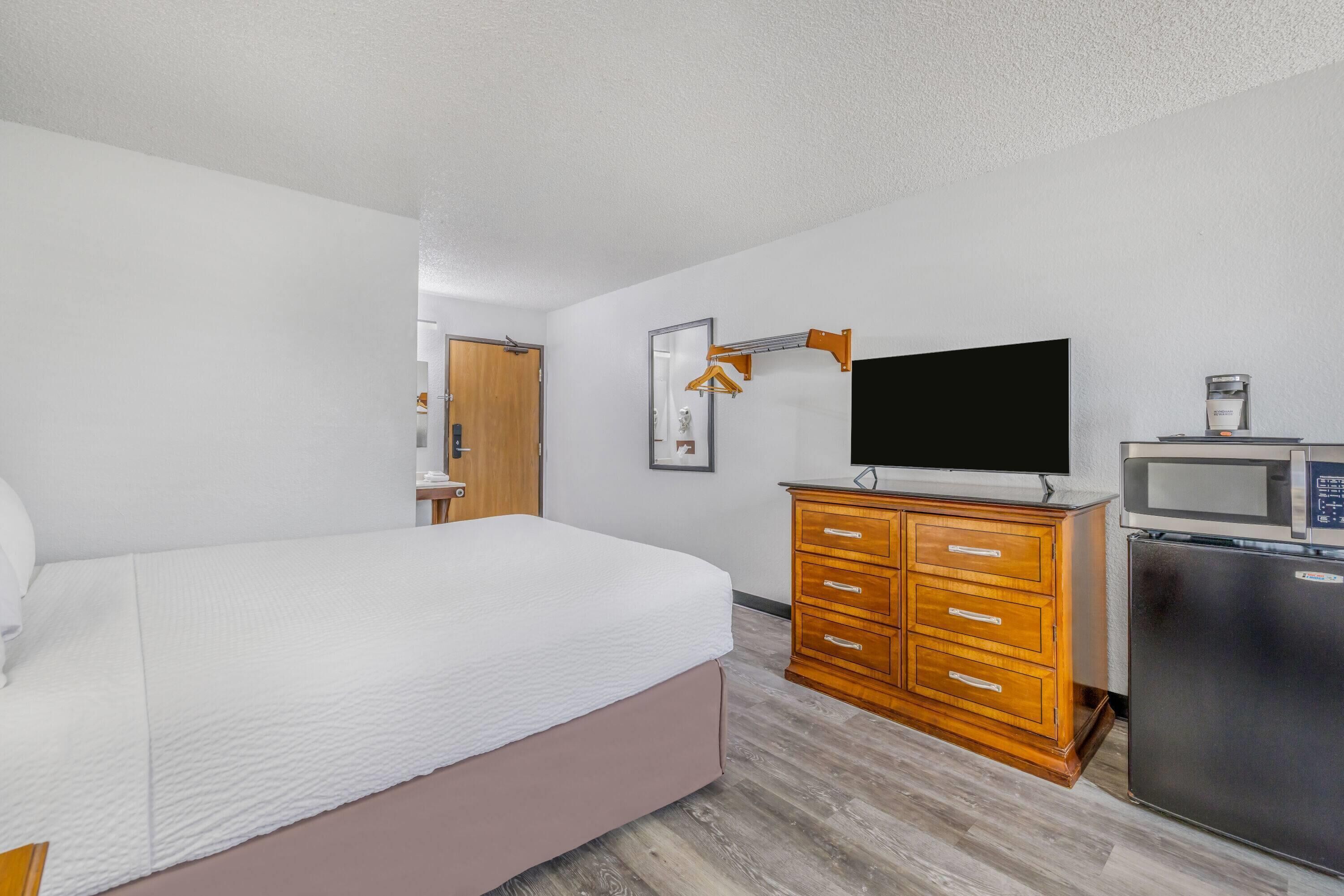 A hotel room with a bed, wooden dresser, TV, and a refrigerator.