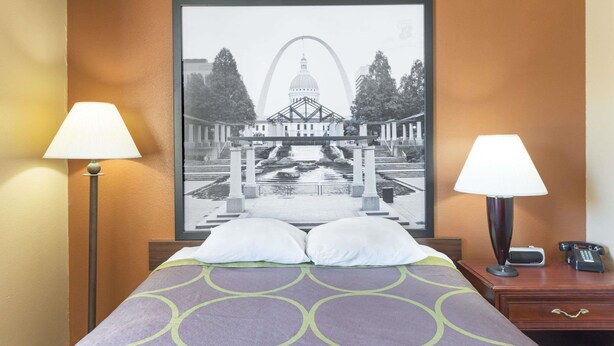 A hotel room with a bed, two bedside lamps, a framed picture of a building, and a nightstand with a phone. - Super 8 by Wyndham Poplar Bluff Missouri (Poplar Bluff)