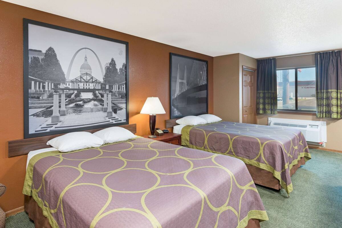 Une chambre d’hôtel avec deux lits, un tableau encadré représentant un pont, une lampe et une fenêtre avec des rideaux.