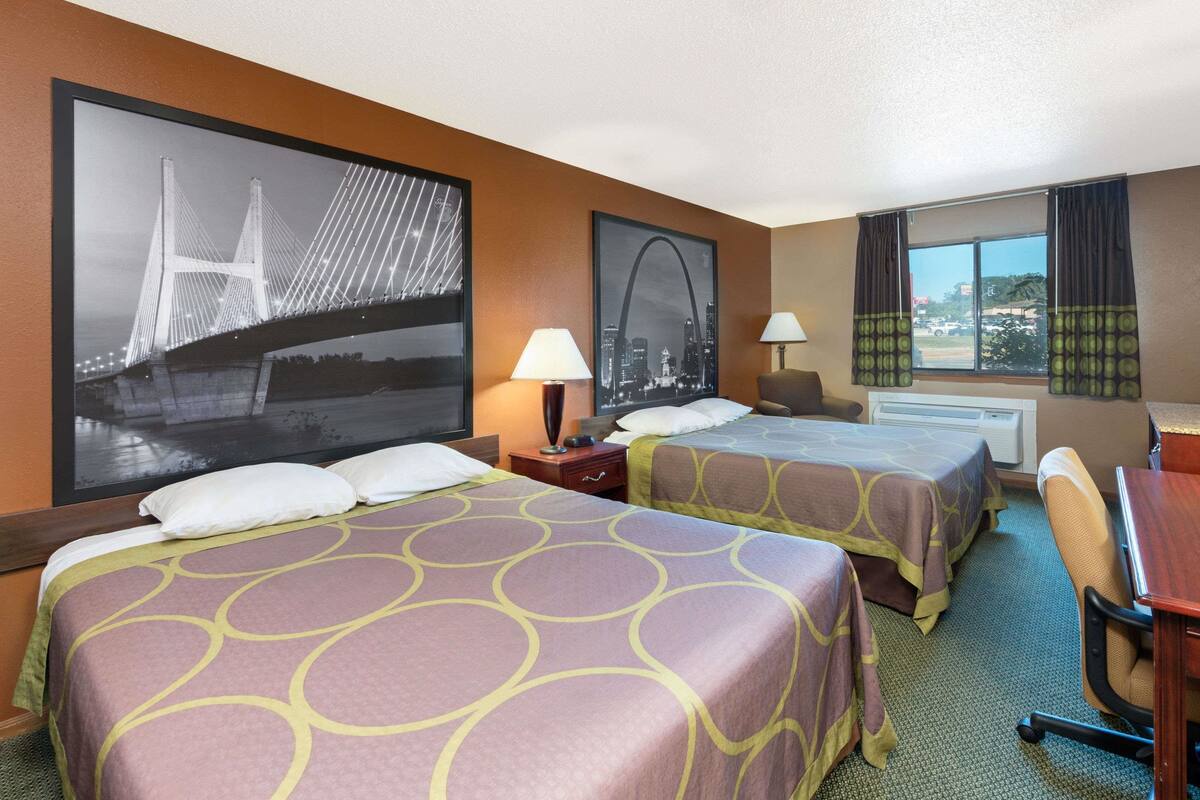 Une chambre d’hôtel avec deux lits, un bureau, une chaise, une fenêtre avec des rideaux et deux lampes fixées au mur.