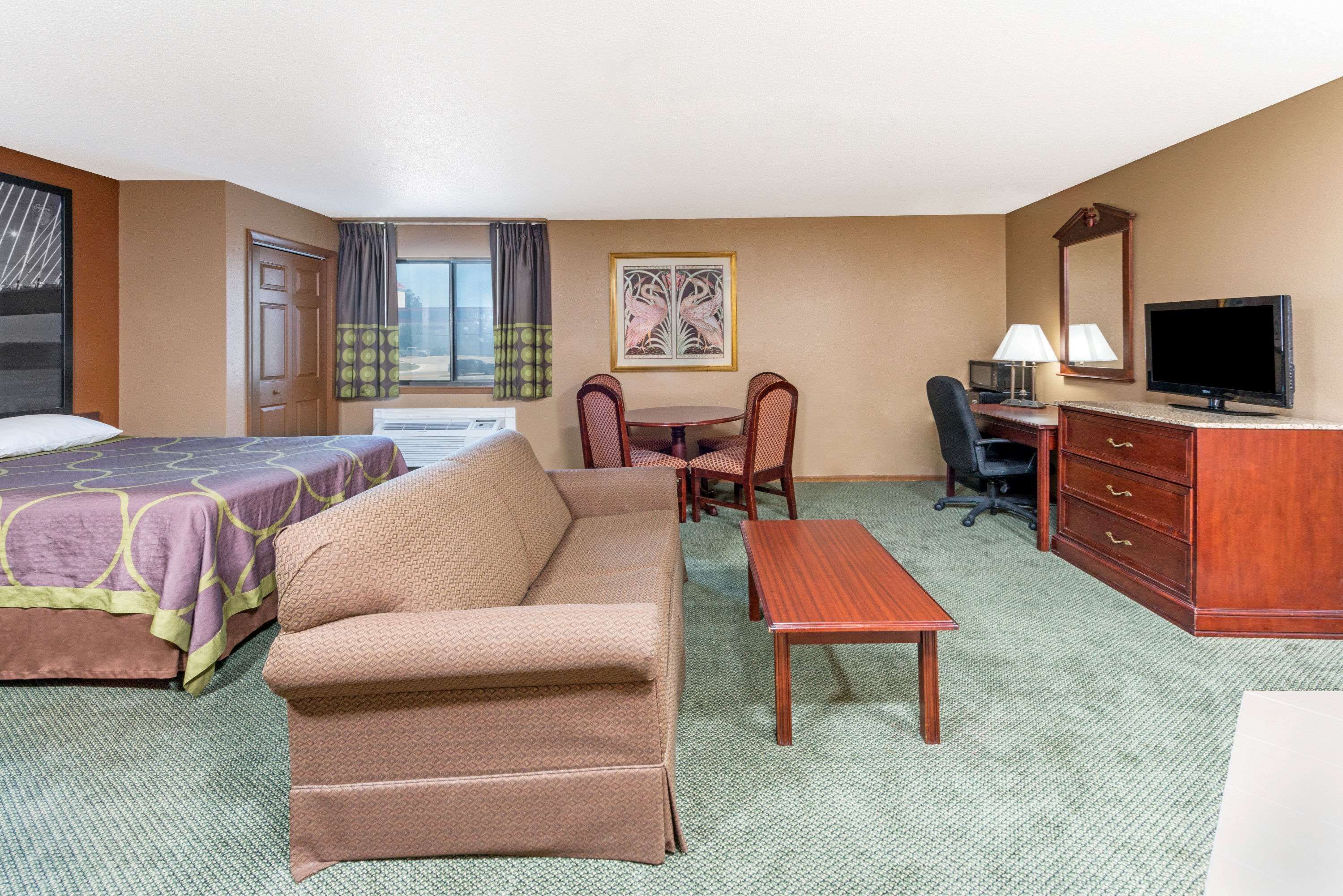Ein Hotelzimmer mit Bett, Sofa, Schreibtisch, Stuhl, Fernseher und einem Bild an der Wand.