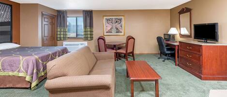 Ein Hotelzimmer mit Bett, Sofa, Schreibtisch, Stuhl, Fernseher und einem Bild an der Wand.
