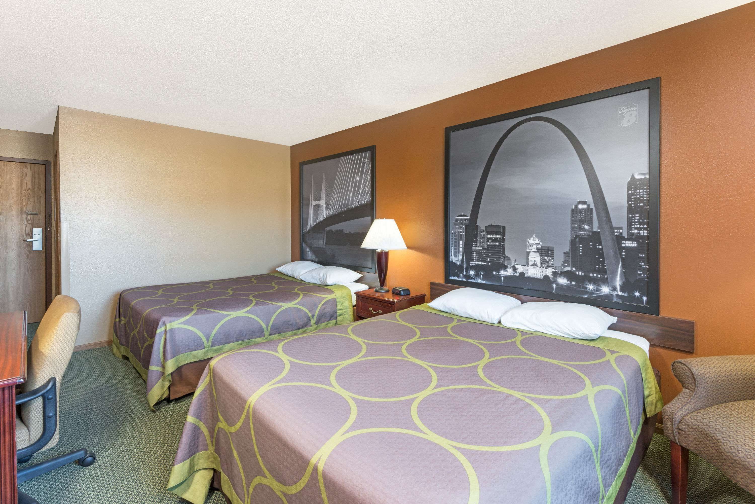 Een hotelkamer met twee bedden, een bureau, een stoel, een lamp en een groot stadsgezichtschilderij aan de muur.