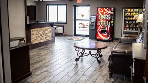 A lobby with a reception desk, a Coca-Cola vending machine, a snack vending machine, and a seating area with a round table. - Super 8 by Wyndham Poplar Bluff Missouri (Poplar Bluff)
