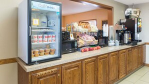 A self-service breakfast area with a refrigerated drink cooler, a coffee machine, and various food items on the counter. - Super 8 by Wyndham Poplar Bluff Missouri (Poplar Bluff)
