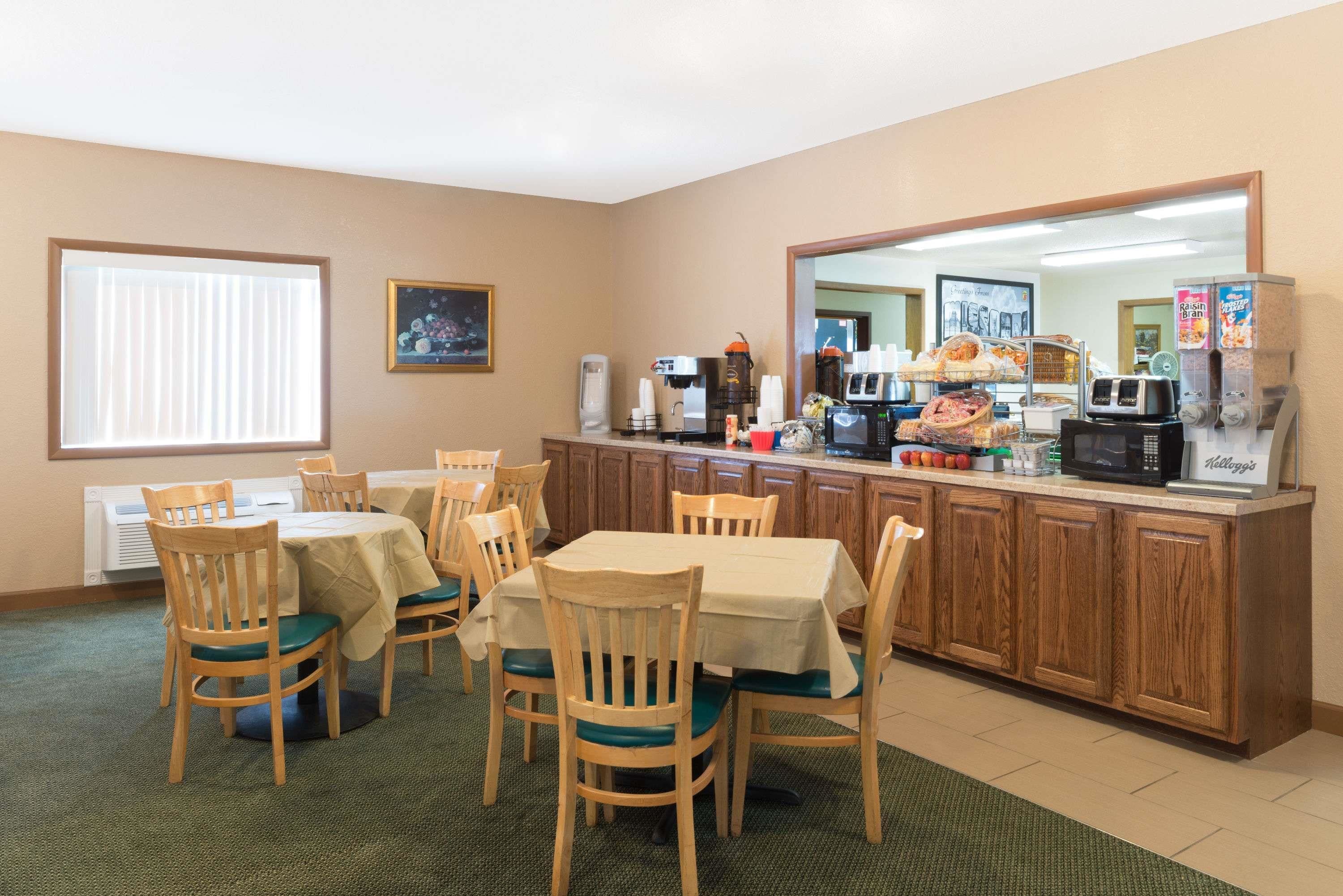 A dining area with wooden chairs and tables, a kitchenette with coffee machines, and a large mirror above the counter.