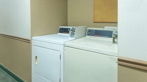 A laundry area with two stacked washers and dryers, a control panel, and a beige wall with a wooden panel above the dryers. - Super 8 by Wyndham Poplar Bluff Missouri (Poplar Bluff)