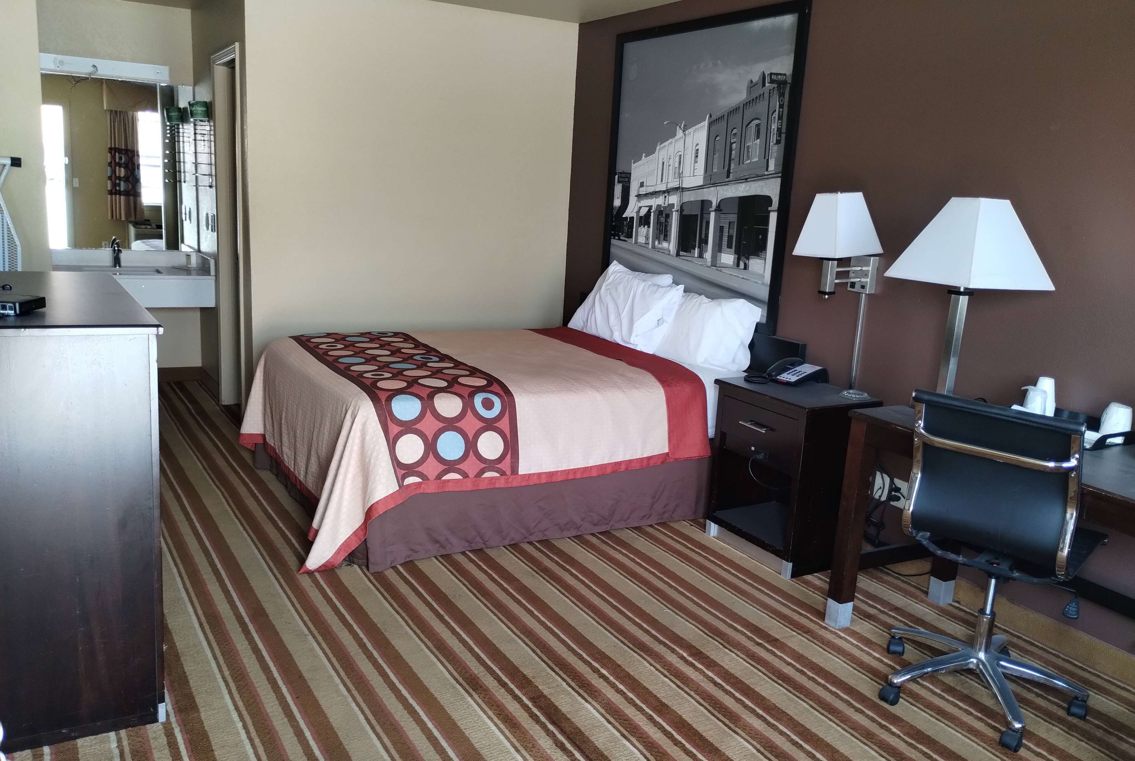 Une chambre d’hôtel avec un lit, un bureau, une chaise, une lampe et une salle de bain visible au fond.