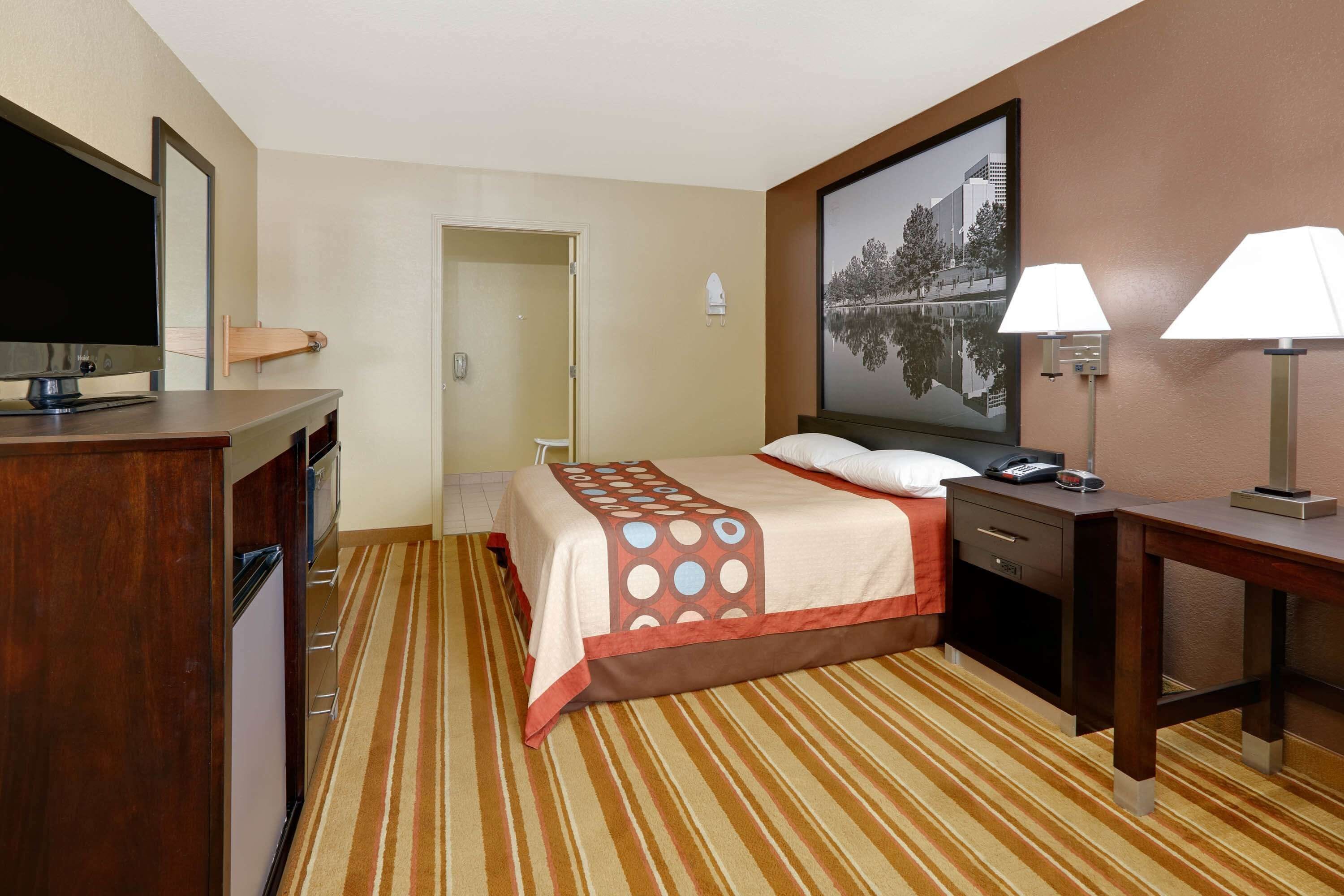 Une chambre d’hôtel comprenant un lit, un bureau, une télévision et une porte donnant accès à une salle de bain.