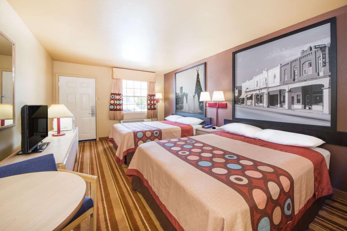 A hotel room with two beds, a desk, a TV, and a large framed picture on the wall.