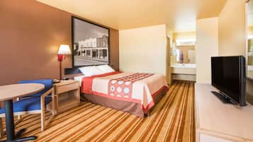 Habitación de hotel con cama, escritorio, silla, televisión y un cuadro en la pared.