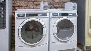 Two white Maytag front-loading washing machines with control panels, placed against a brick wall.