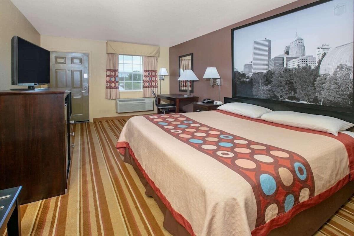 A hotel room with a large bed, a desk, a chair, a TV, and a window with a cityscape view.
