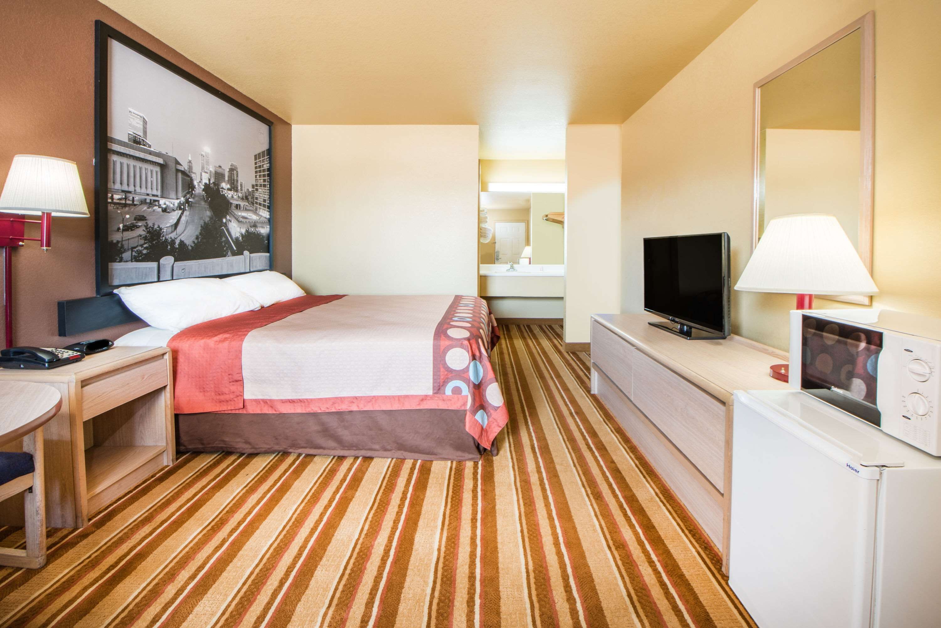 Habitación de hotel con cama, escritorio, televisión, espejo y piso alfombrado.