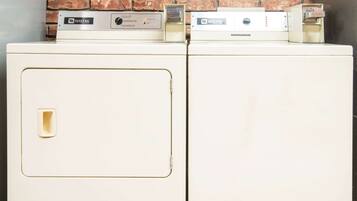 A white washing machine with a Maytag label, placed against a brick wall.