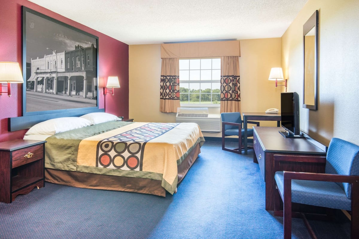 A hotel room with a bed, desk, chair, and a large window with curtains.