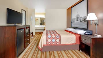A hotel room with a bed, a TV, a desk, a lamp, and a painting on the wall.