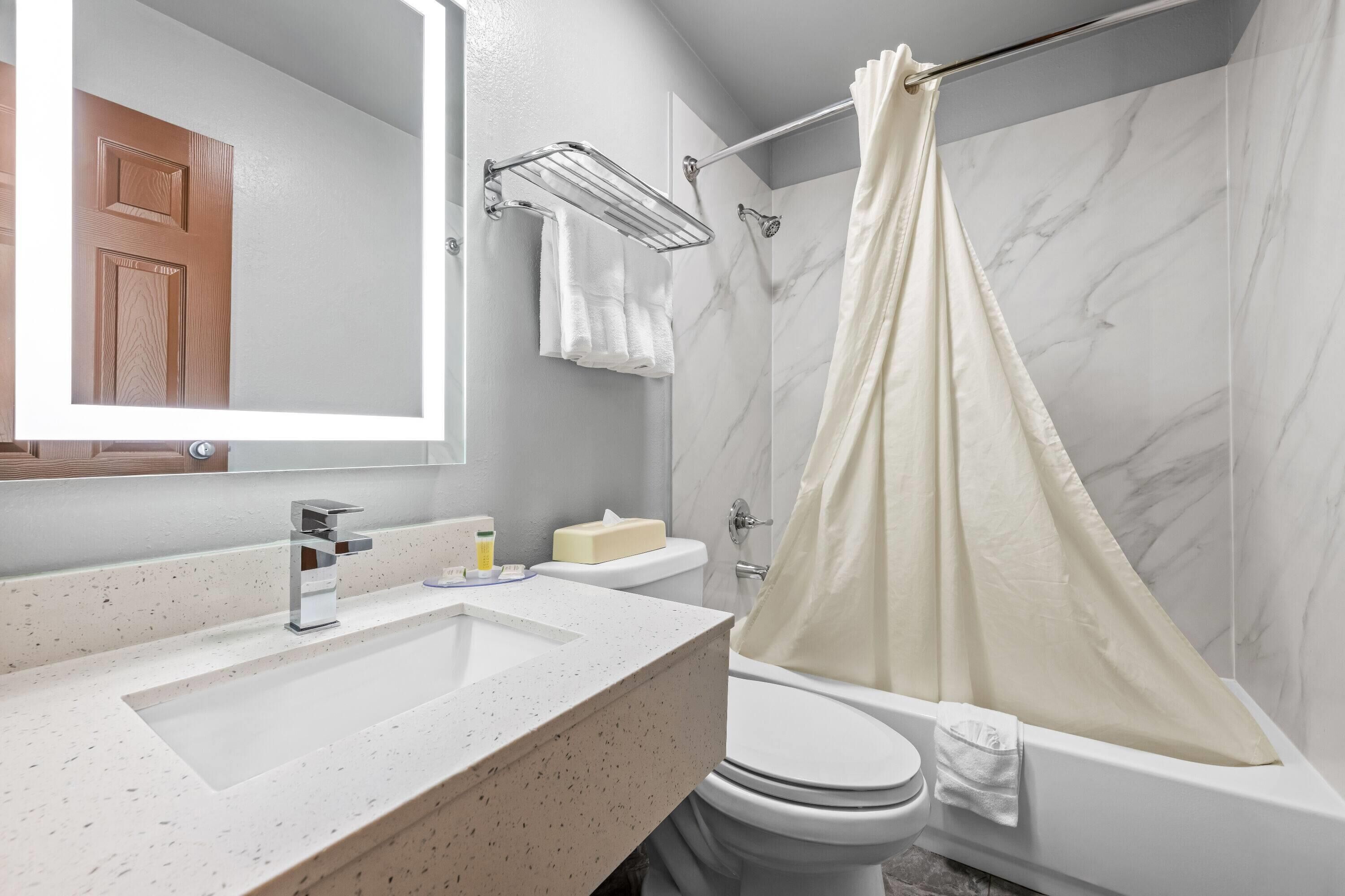 A bathroom with a marble wall, a white sink, a toilet, and a shower curtain.