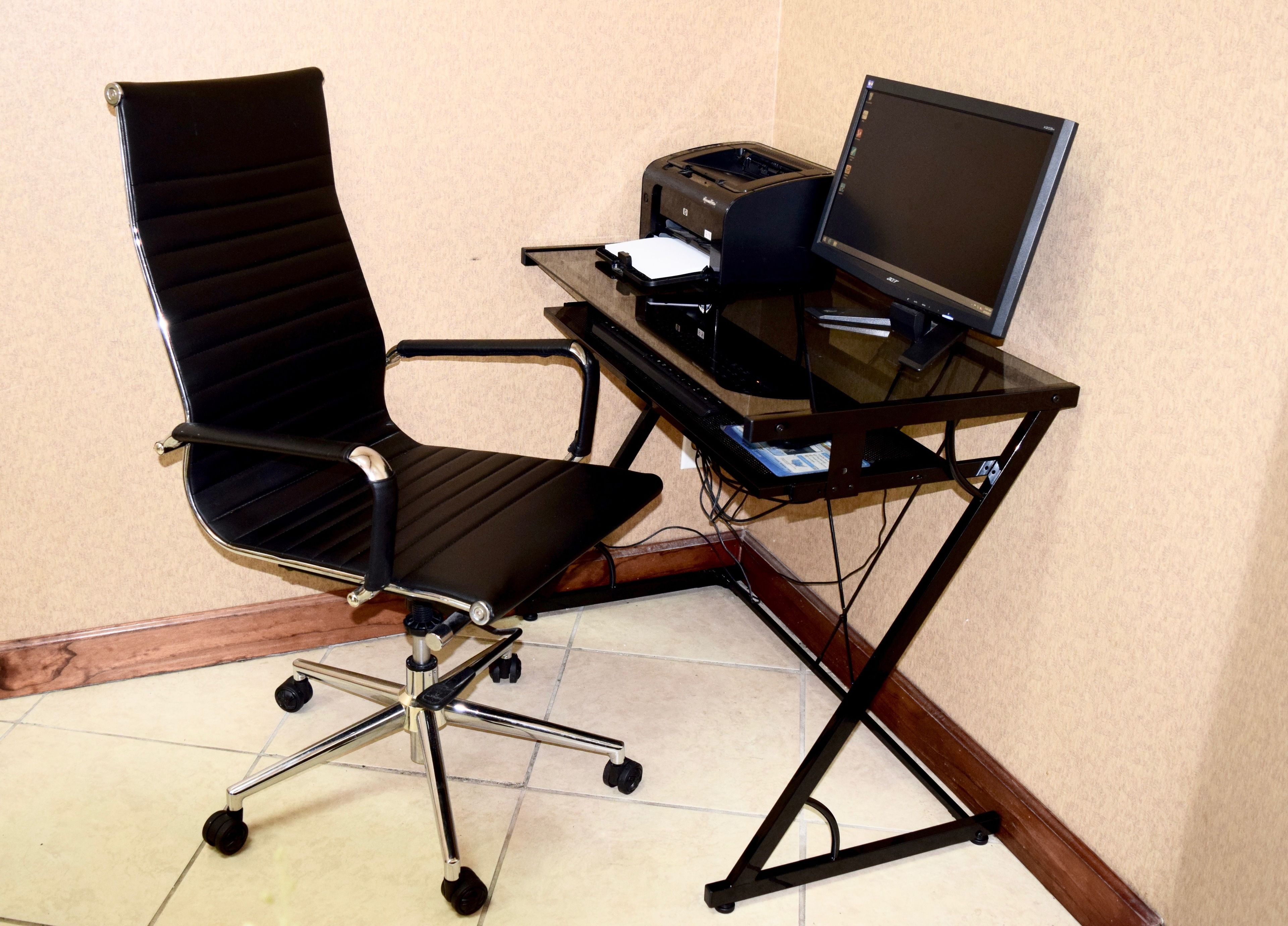 Un bureau d’angle aménagé avec un fauteuil pivotant, un ordinateur de bureau et une imprimante posés sur le bureau.