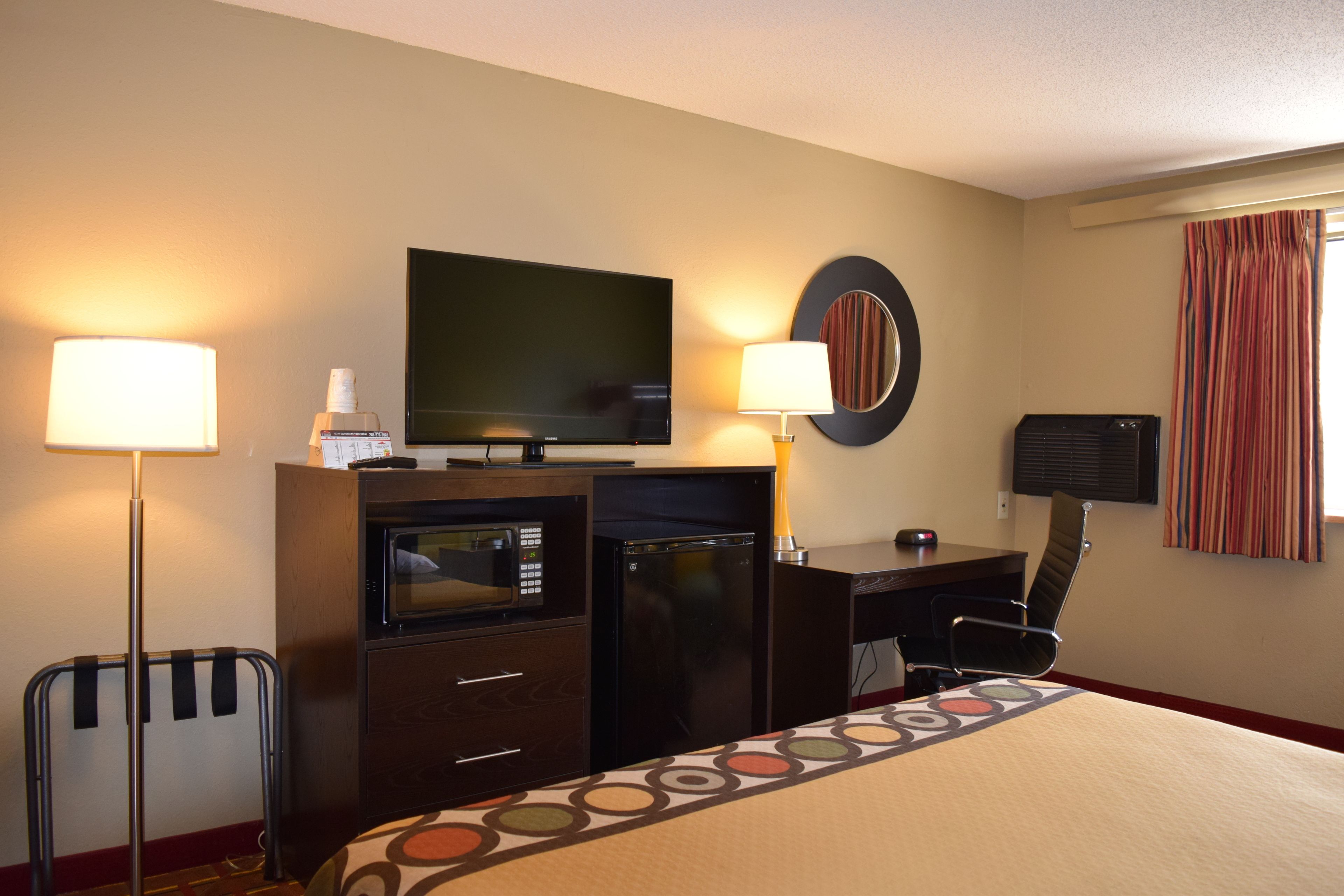 Ein Hotelzimmer mit einem Bett, einem Schreibtisch mit Computer, einem Fernseher, einer Mikrowelle und einem Kühlschrank.