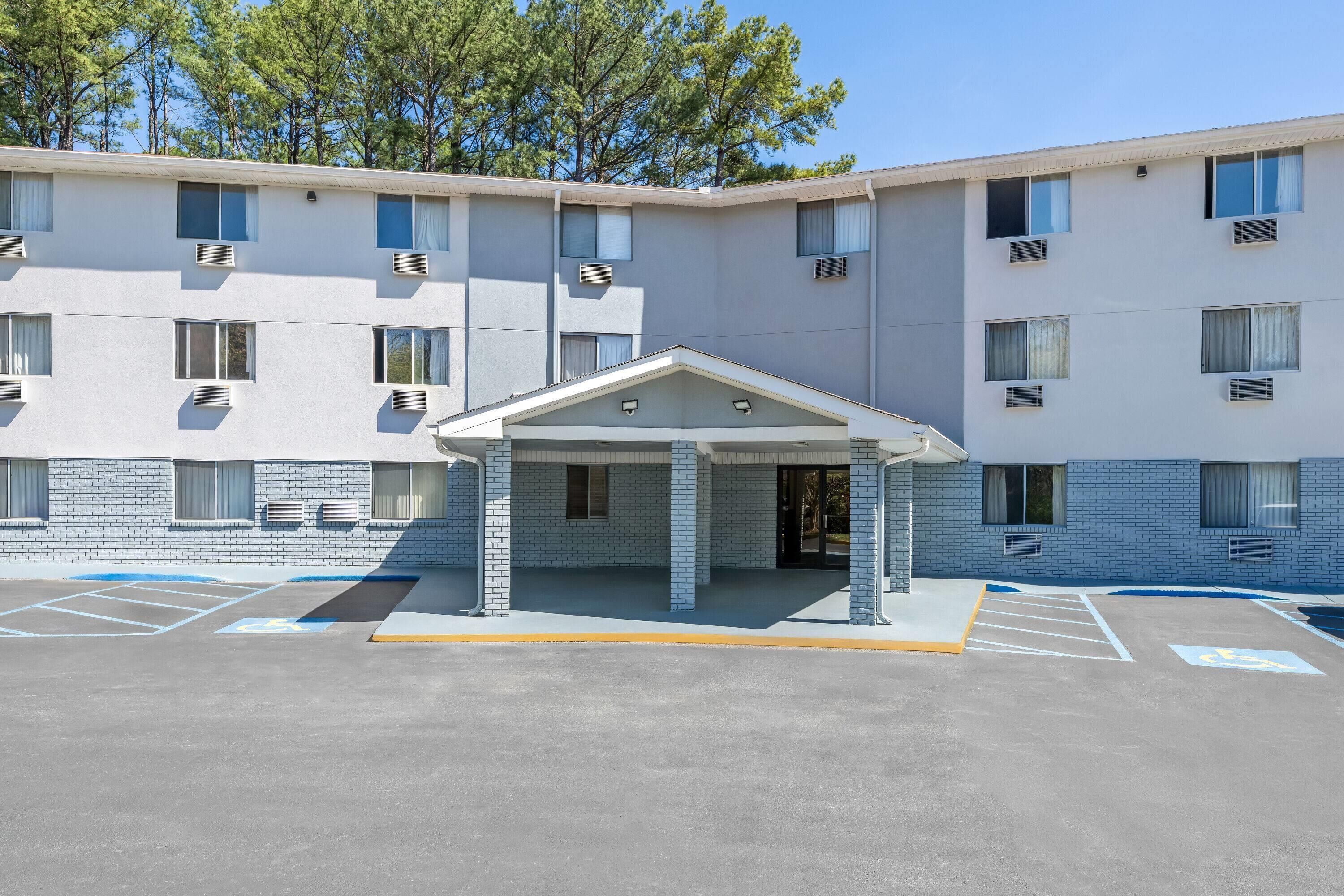 A multi-story building with a covered entrance, parking lot with marked spaces, and a clear sky.