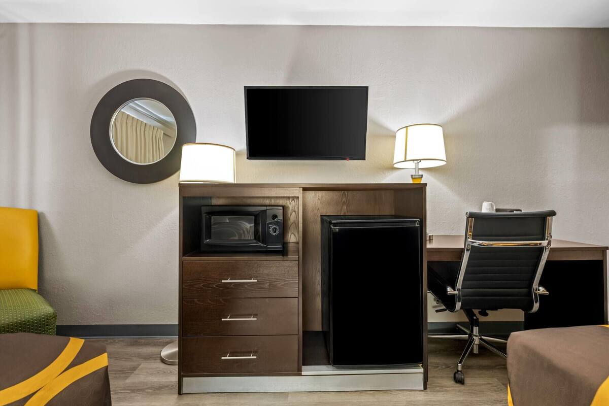 Habitación de hotel con escritorio de madera, televisor de pantalla plana, microondas, refrigerador, una silla y una cama.