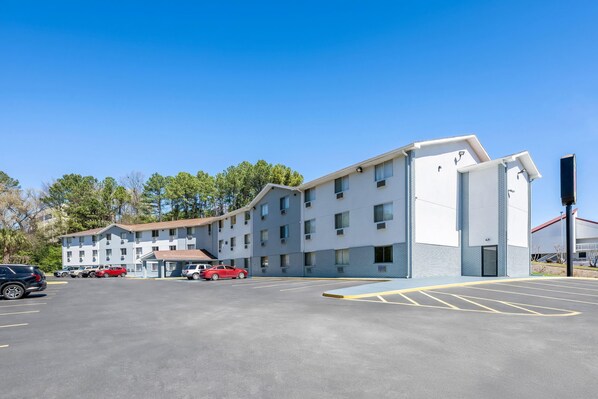 Un hotel a più piani con un parcheggio, diverse auto parcheggiate e un cielo azzurro intenso.