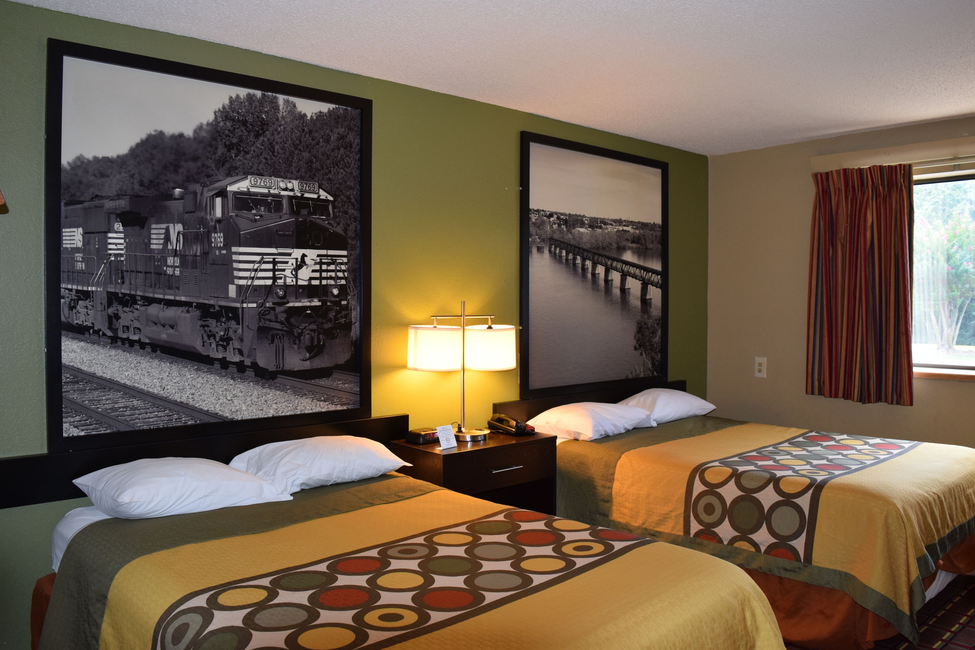 A hotel room with two beds, a nightstand with a lamp, and two framed pictures on the wall.