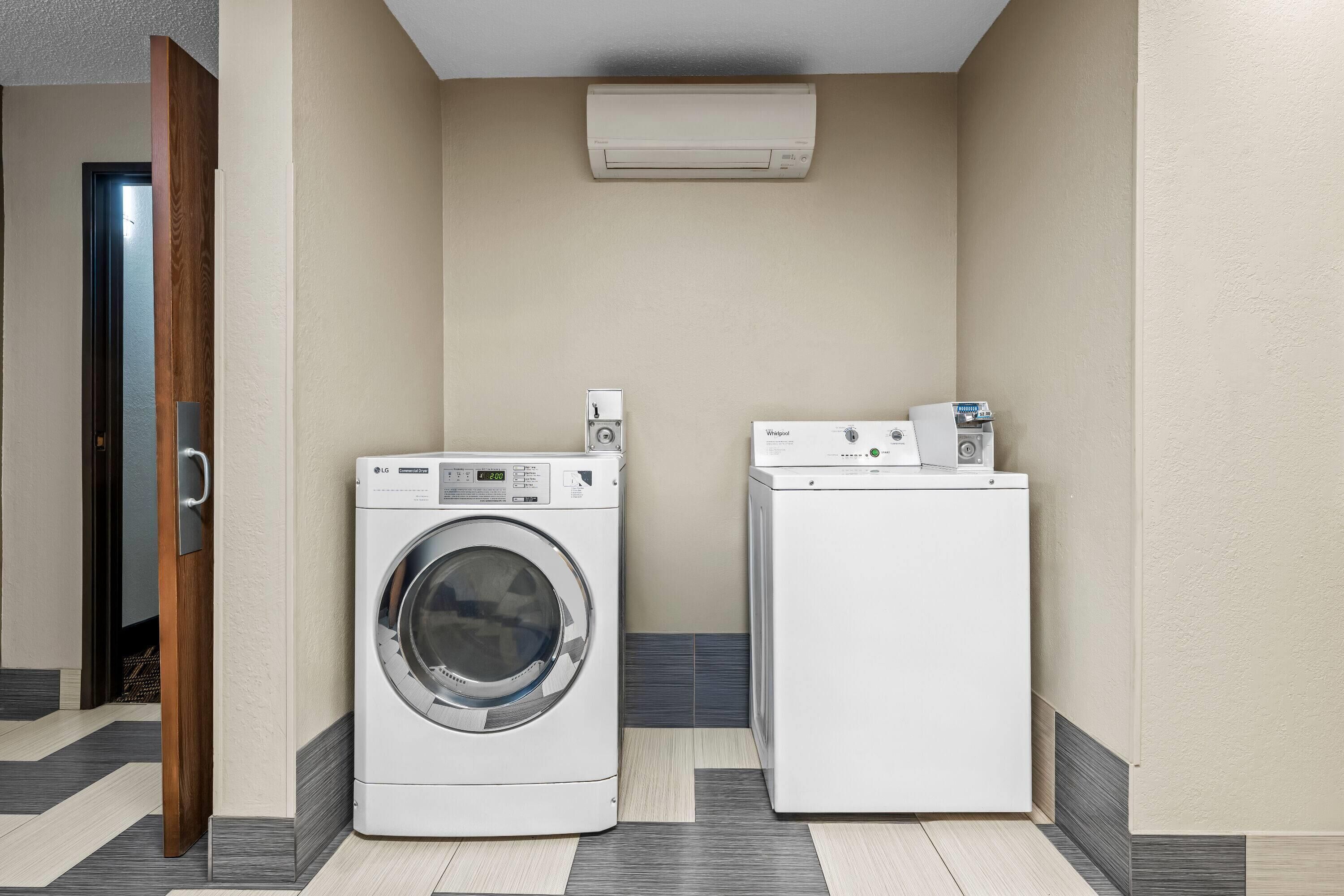 A laundry room with two washing machines, a wooden door, and an air conditioning unit.