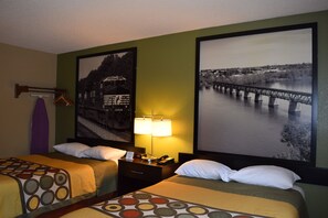 Una camera d'albergo con due letti, un comodino con una lampada e due quadri di grandi dimensioni appesi al muro.