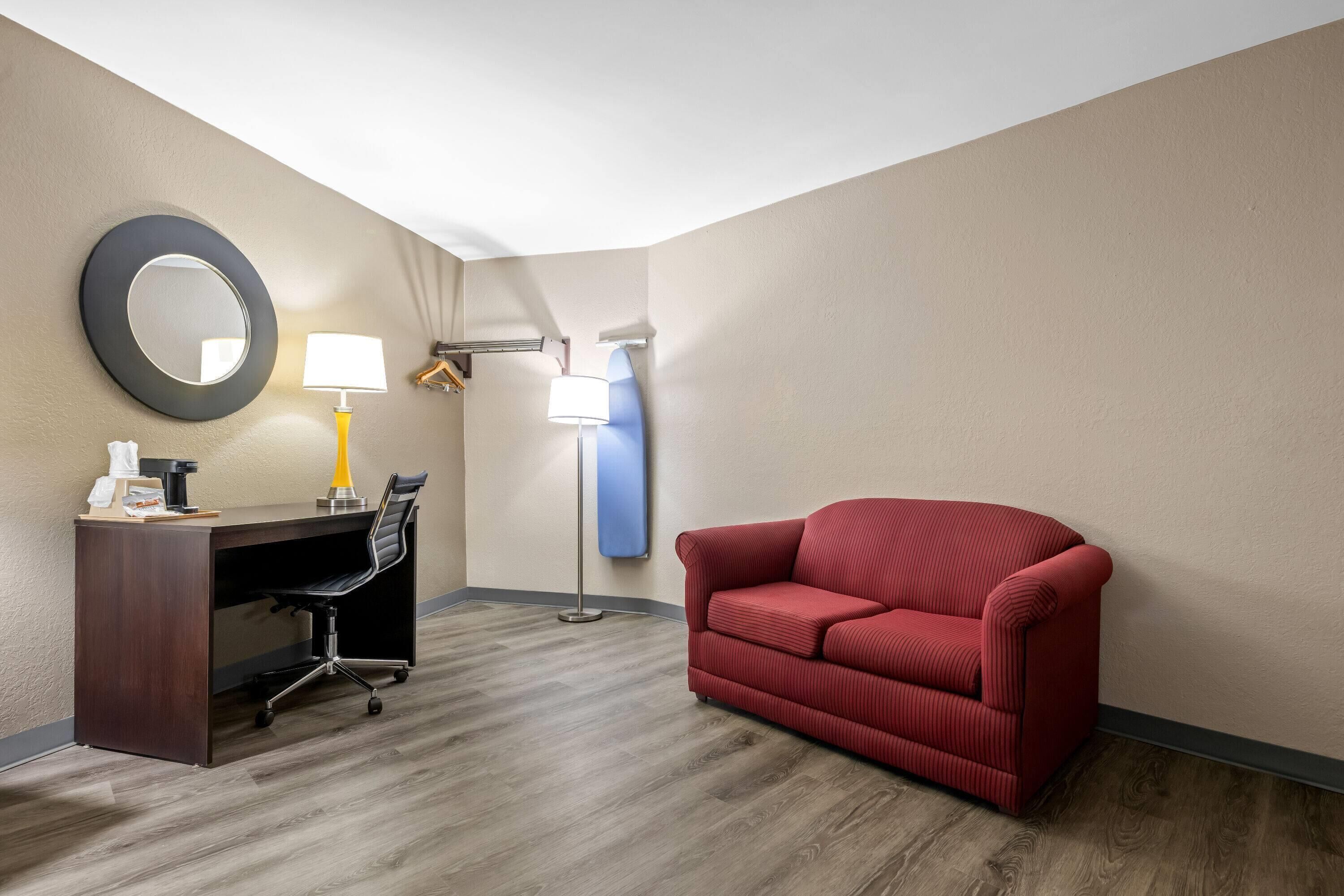 Une chambre d’hôtel équipée d’un bureau, d’une chaise, d’un canapé rouge et de deux lampes fixées au mur.