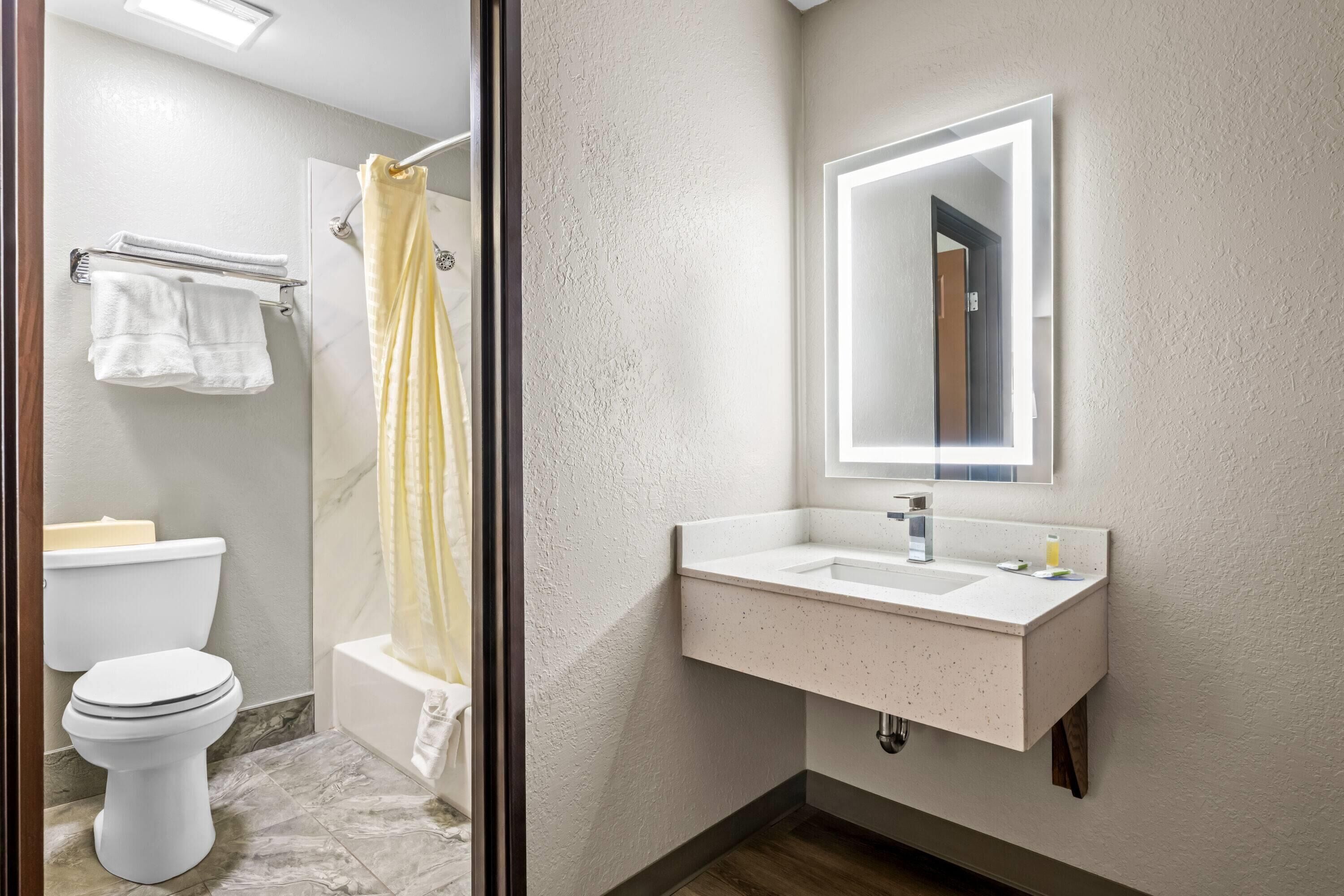 A bathroom with a toilet, bathtub, shower curtain, sink, and mirror.