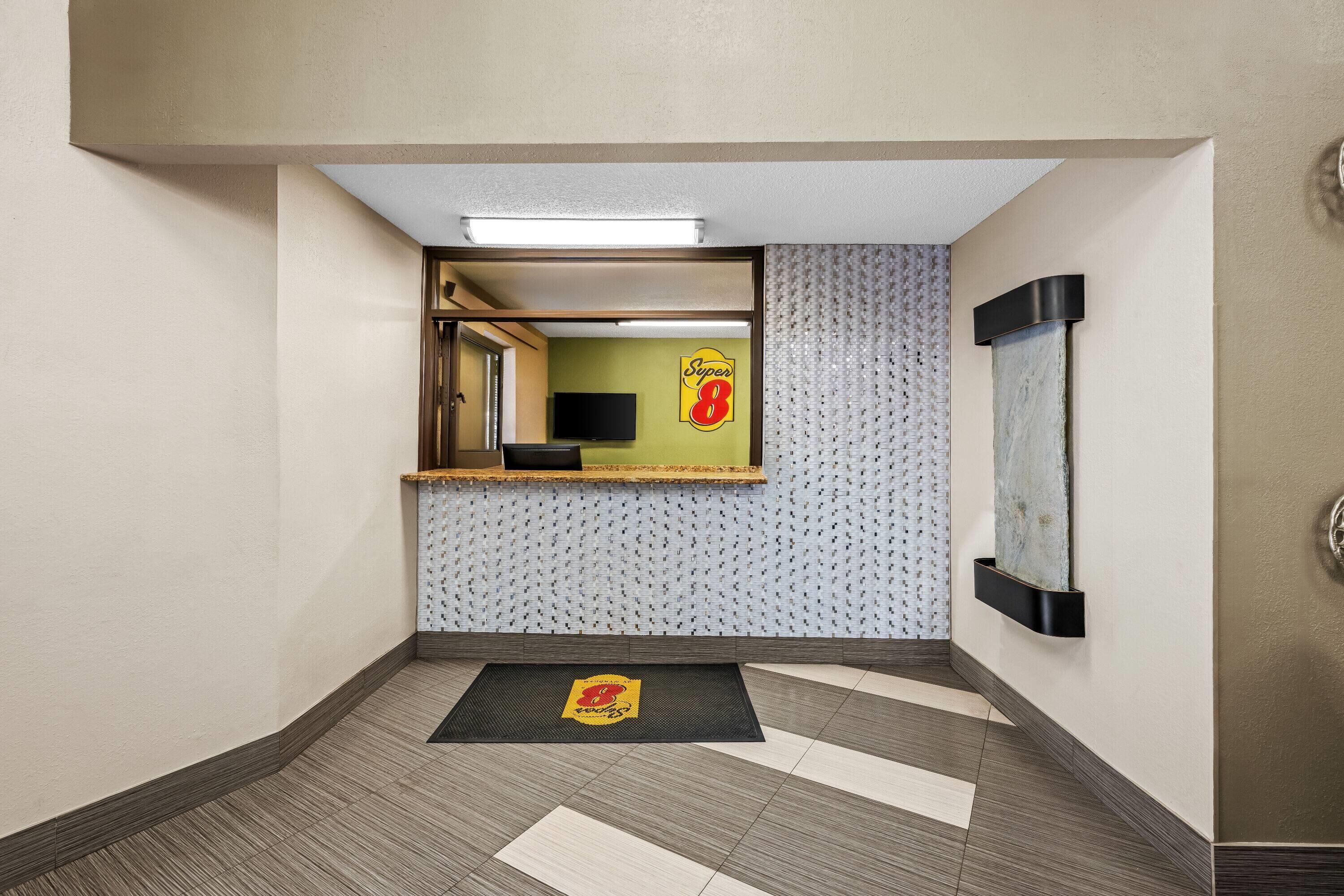 Een hotellobby met een receptiebalie, een behang met patroon en een incheckruimte.