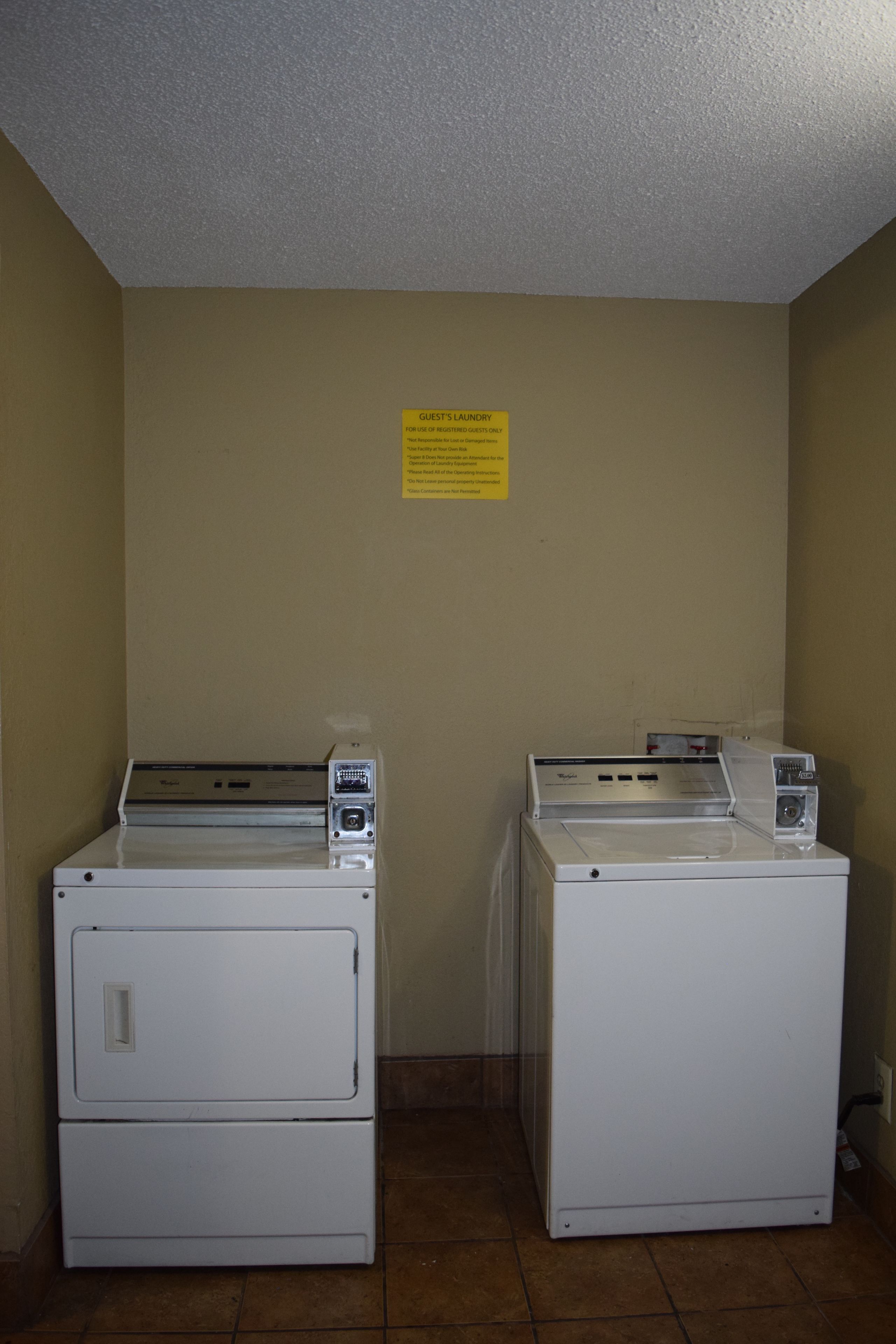A laundry area with two stacked washers and dryers, a yellow sign above them, and a tiled floor.