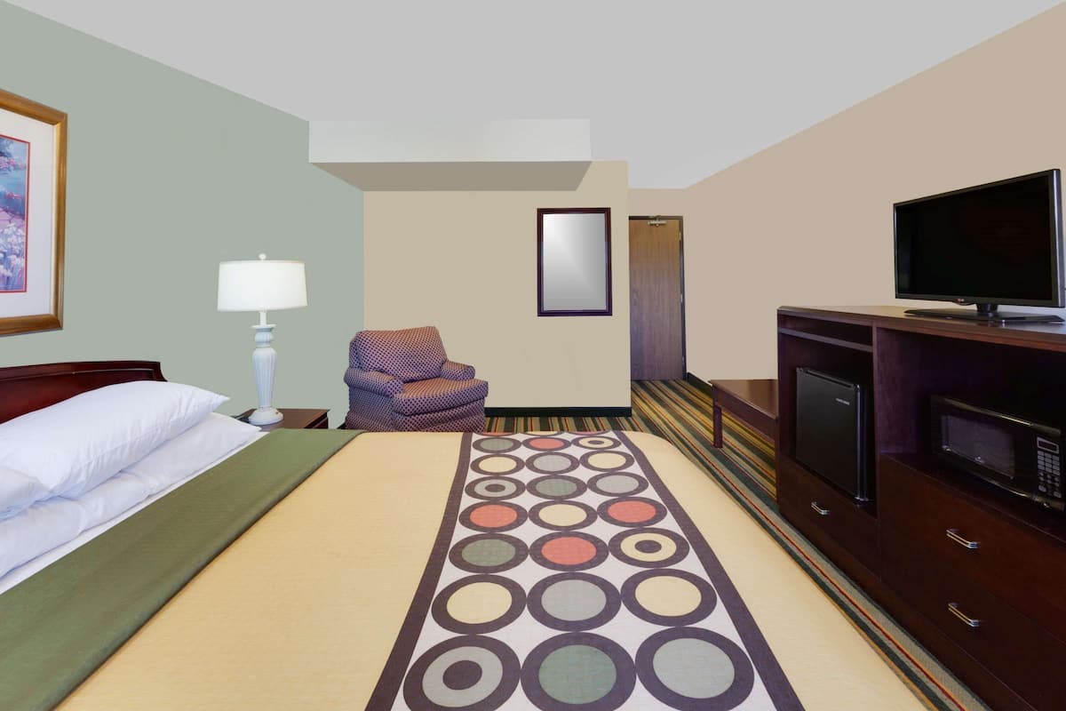 A hotel room with a bed, a chair, a TV, a microwave, and a cabinet.