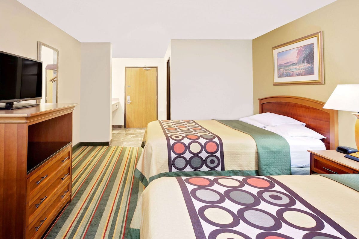 A hotel room with two beds, a TV, a desk, and a painting on the wall.
