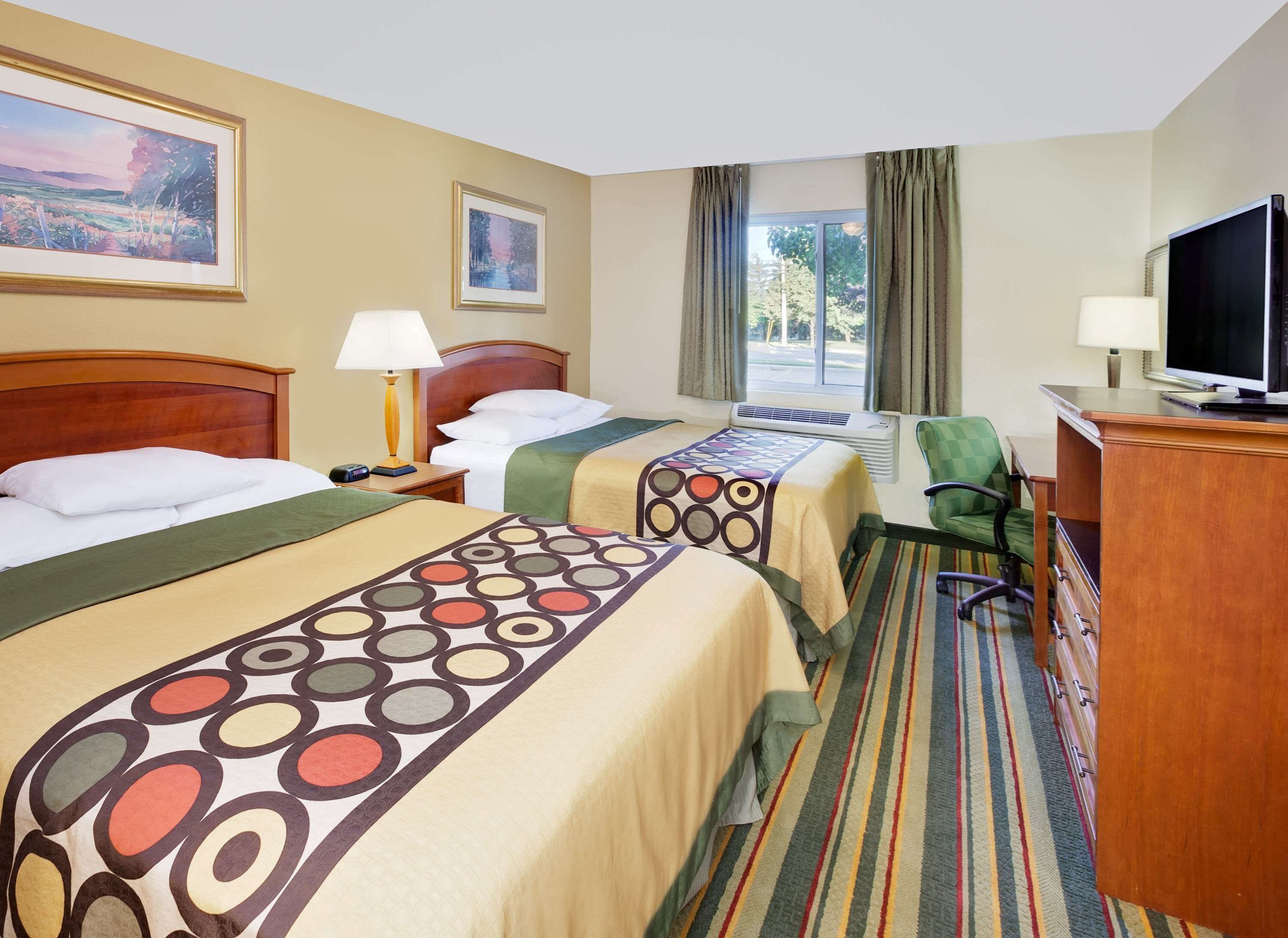 A hotel room with two beds, a desk, a television, and a window with curtains.
