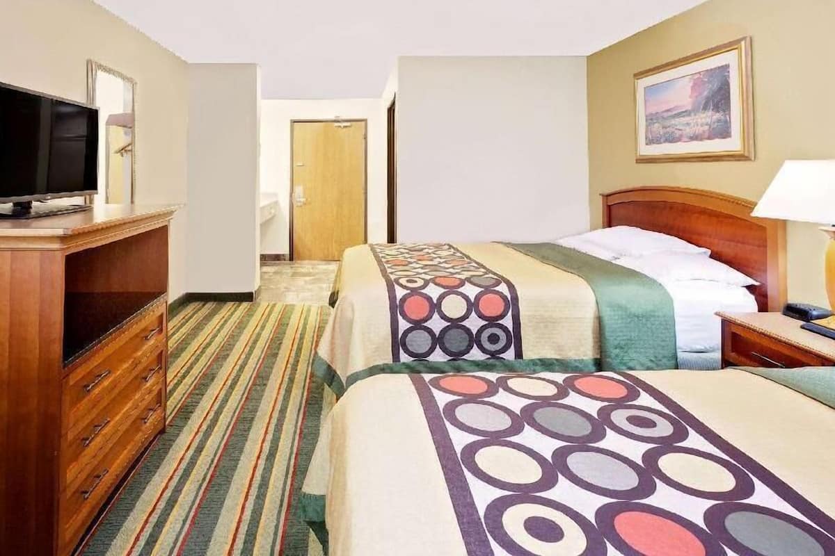 A hotel room with two beds, a television, a dresser, and a painting on the wall.