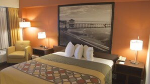Habitación de hotel con una cama grande, dos lámparas de noche, una silla y un cuadro de un muelle en la pared.