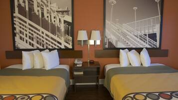 A hotel room with two beds, a nightstand with a lamp, and two framed pictures on the wall.