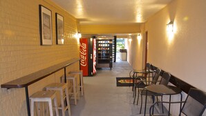 Un pasillo con una máquina expendedora de Coca-Cola, taburetes de madera y sillas de metal.