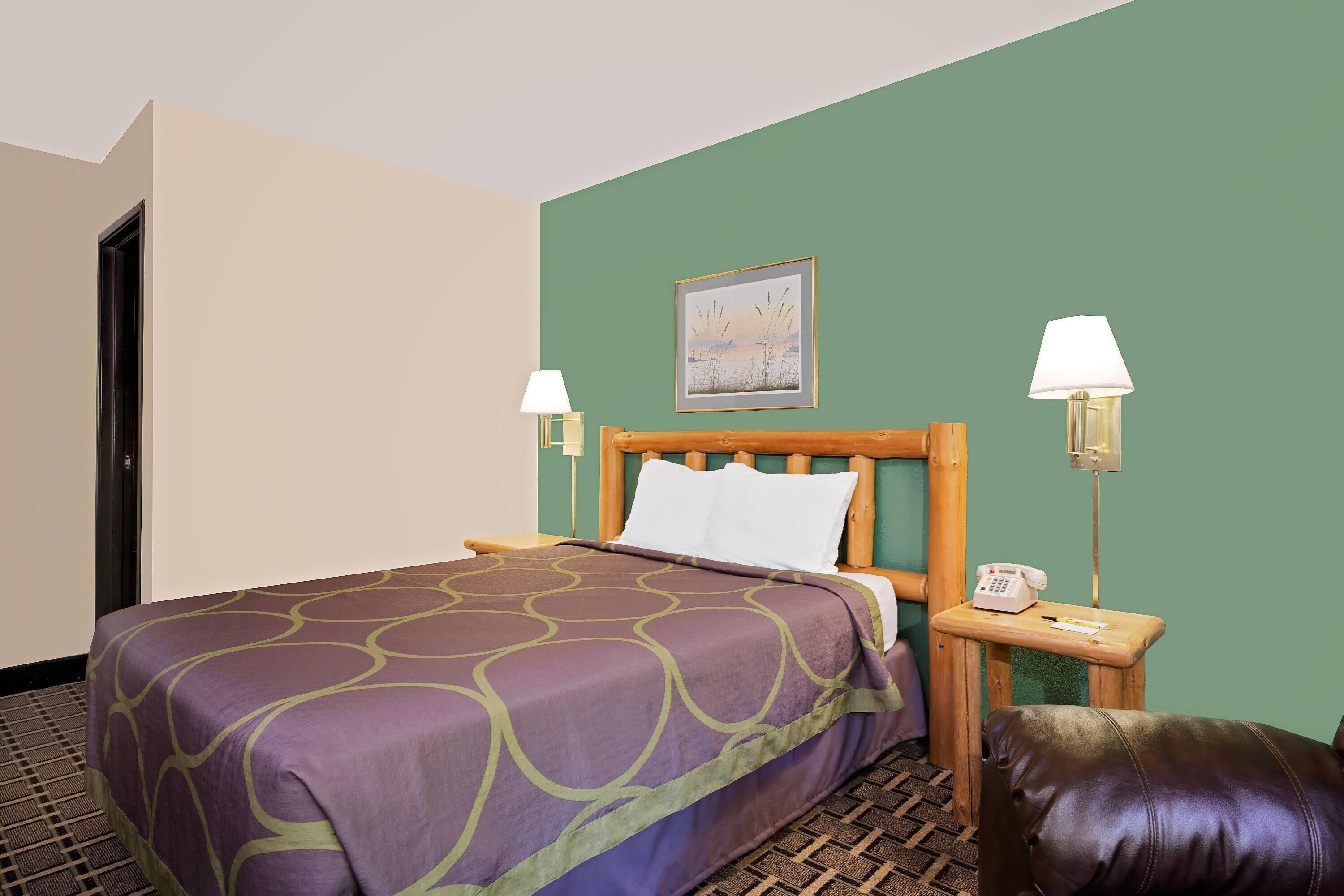 A hotel room with a bed, a wooden headboard, two bedside lamps, a telephone, a pillow, and a green wall.