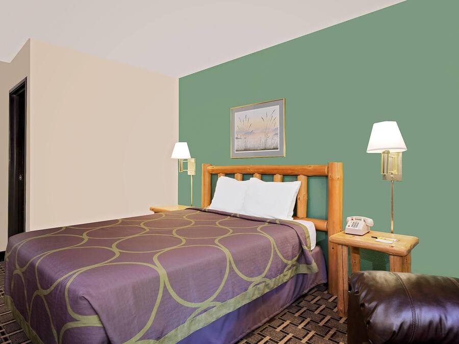 A hotel room with a bed, a wooden headboard, two bedside lamps, a telephone, a pillow, and a green wall.
