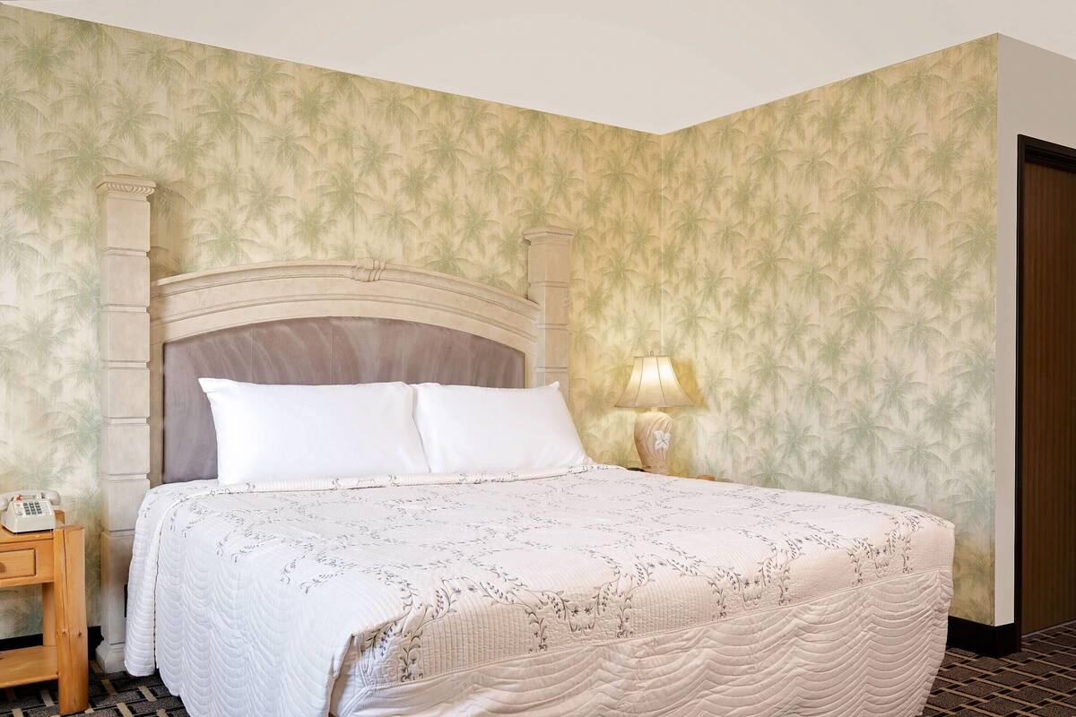 Una cama bien hecha con cabecera, una lámpara de noche y un teléfono sobre una mesita de madera.