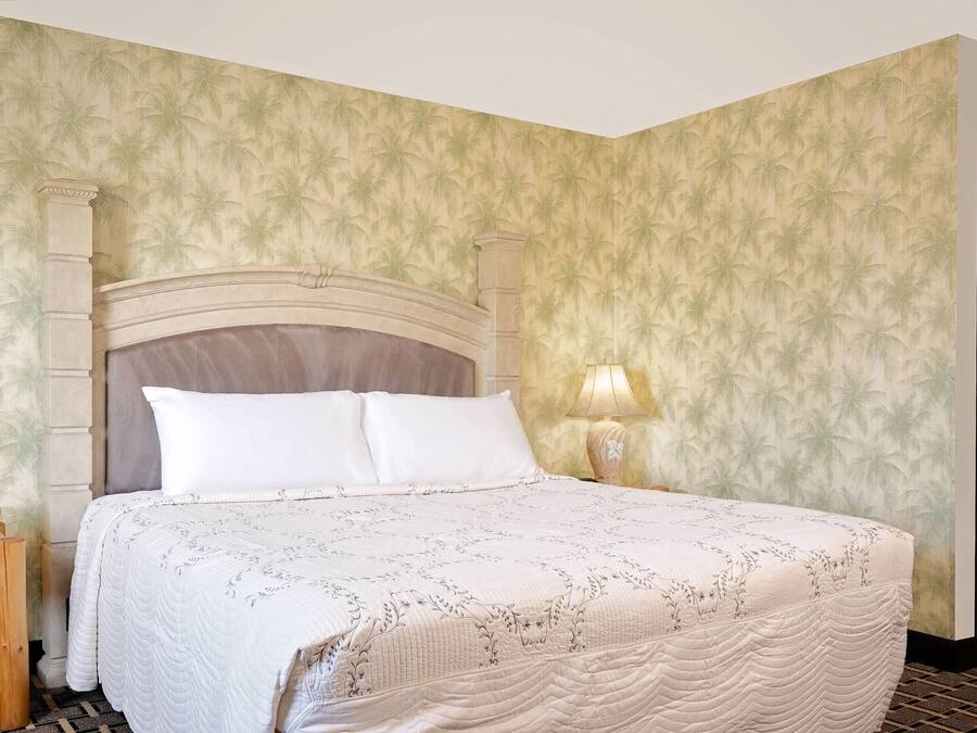 Una cama bien hecha con cabecera, una lámpara de noche y un teléfono sobre una mesita de madera.