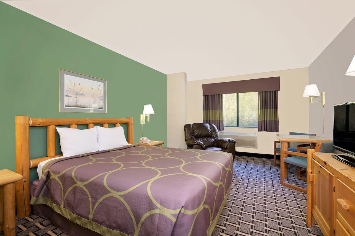 Habitación de hotel con cama, escritorio, silla, televisor y ventana con cortinas.